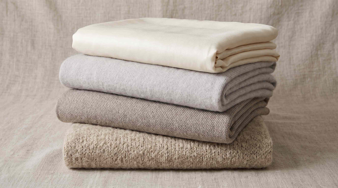 Four folded luxury throw blankets in different fibers, stacked to compare texture and material.